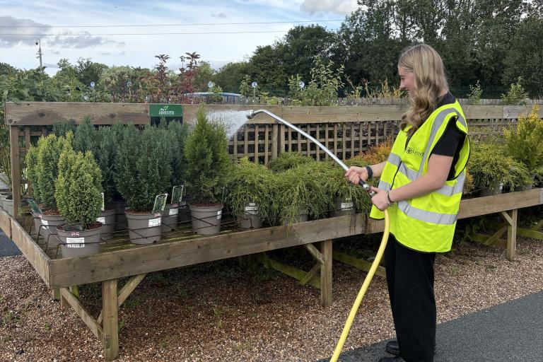 A woman in a high vis jacket waters plants with a hose