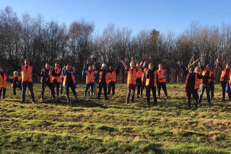 Image shows large group of volunteers in a field smiling and waving to camera