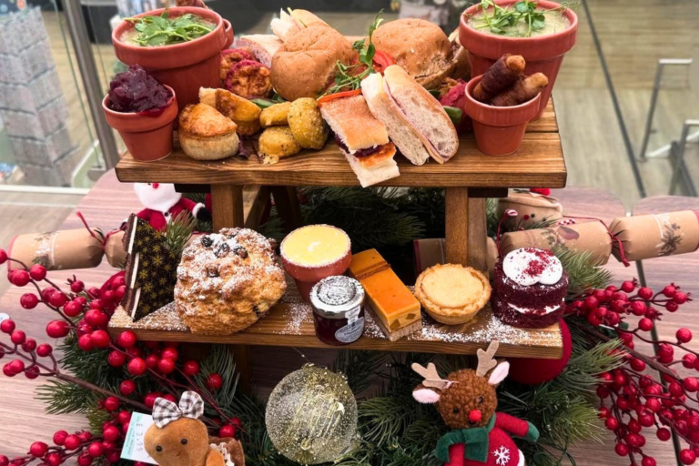 A festive afternoon tea, a selection of sweet and savoury snacks are placed on a wooden display, surrounded by Christmas decorations.