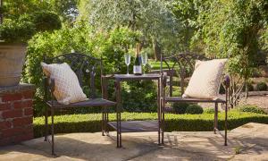 Image shows two garden chairs in-between a table with a bottle and two glasses