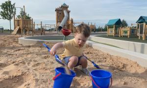 Image shows child playing with a bucket and spade in the sand at Fun Arium